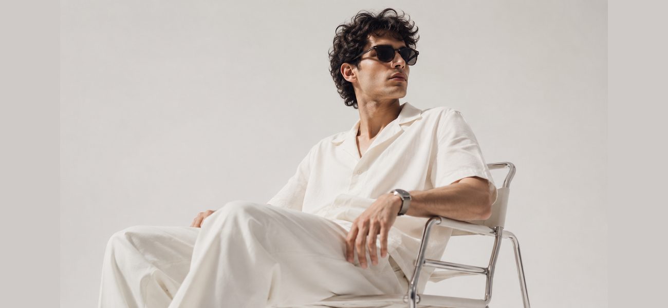 Man in a white linen summer outfit seated on a chrome chair
