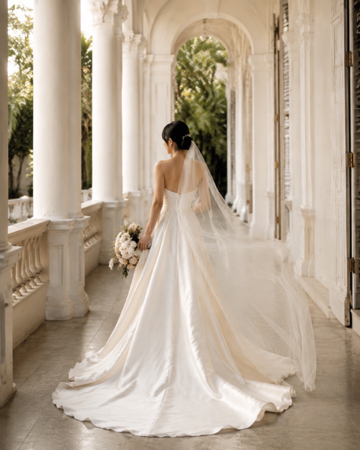 Bride walking a white colonnade with her veil trailing behind her
